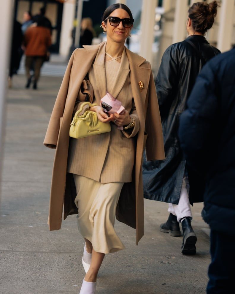 Chic Layering: Camel Coat over Beige Knit and Satin Skirt Chic Layering: Camel Coat over Beige Knit and Satin Skirt — Interview Outfits 2027