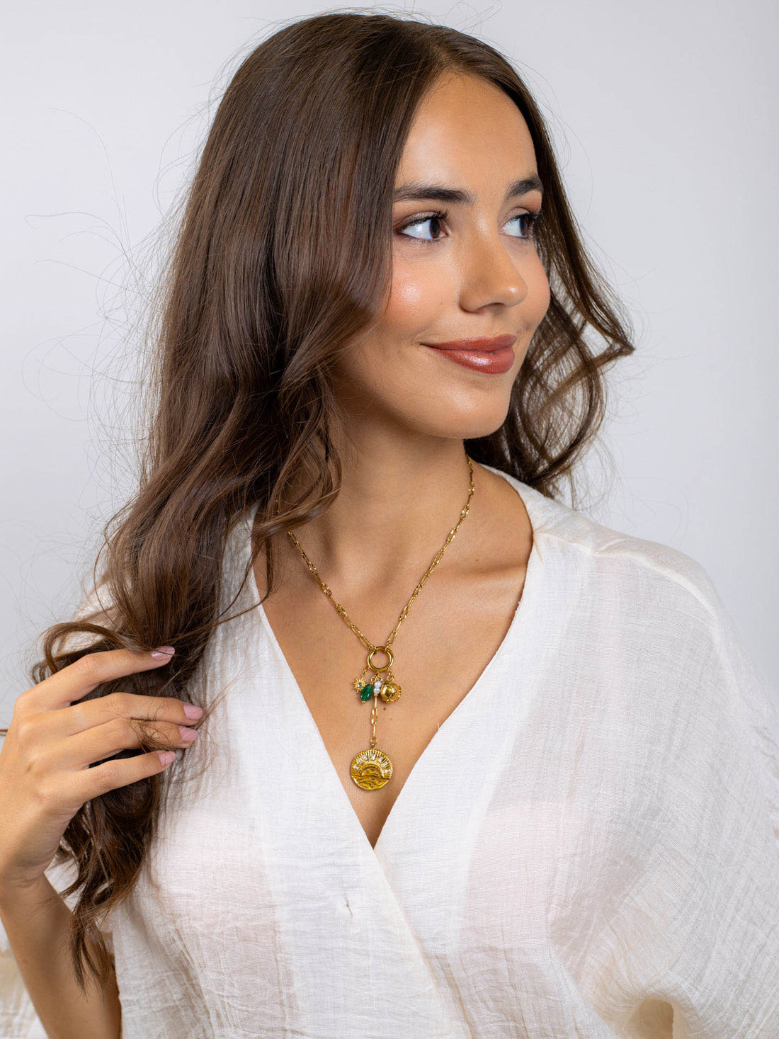 Layered Gold Pendants and Green Stone Accents Over a White Wrap Top Layered Gold Pendants and Green Stone Accents Over a White Wrap Top — Locket Necklaces 2027