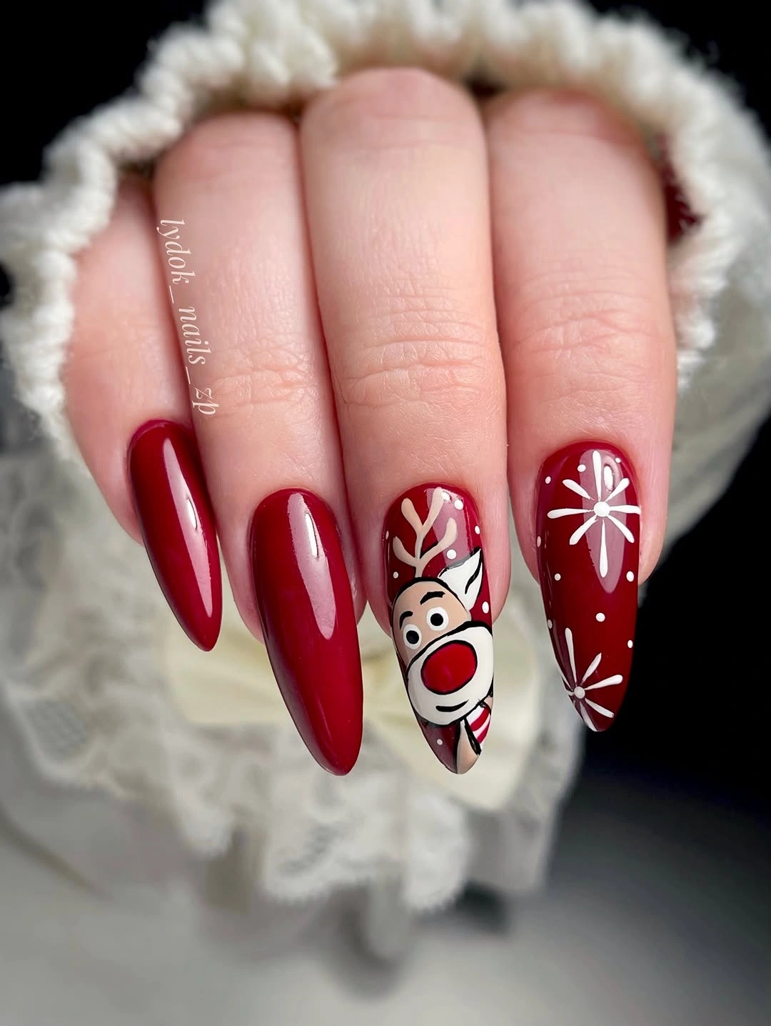 Red Almond Nails With Reindeer and White Starbursts Long red almond nails with reindeer and white starburst details
